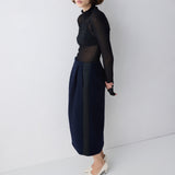 Woman wearing a black sheer top and navy skirt against a white background