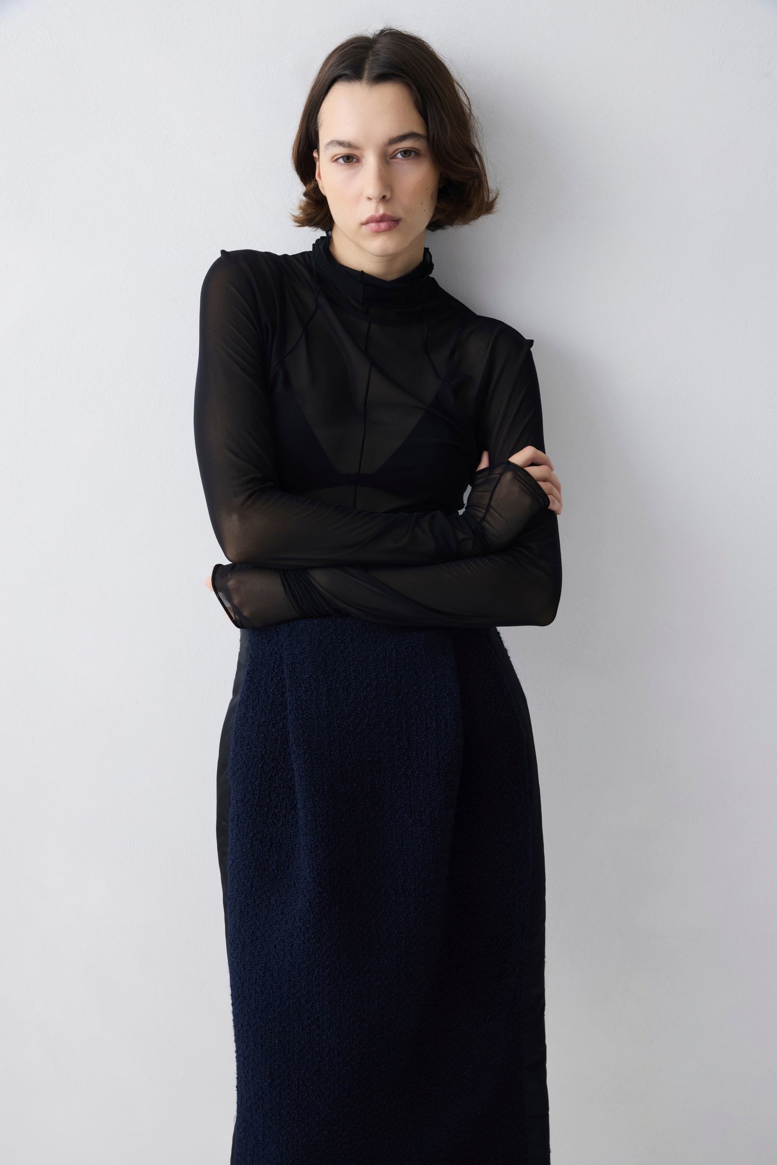 Woman wearing a black top and navy skirt against a white background