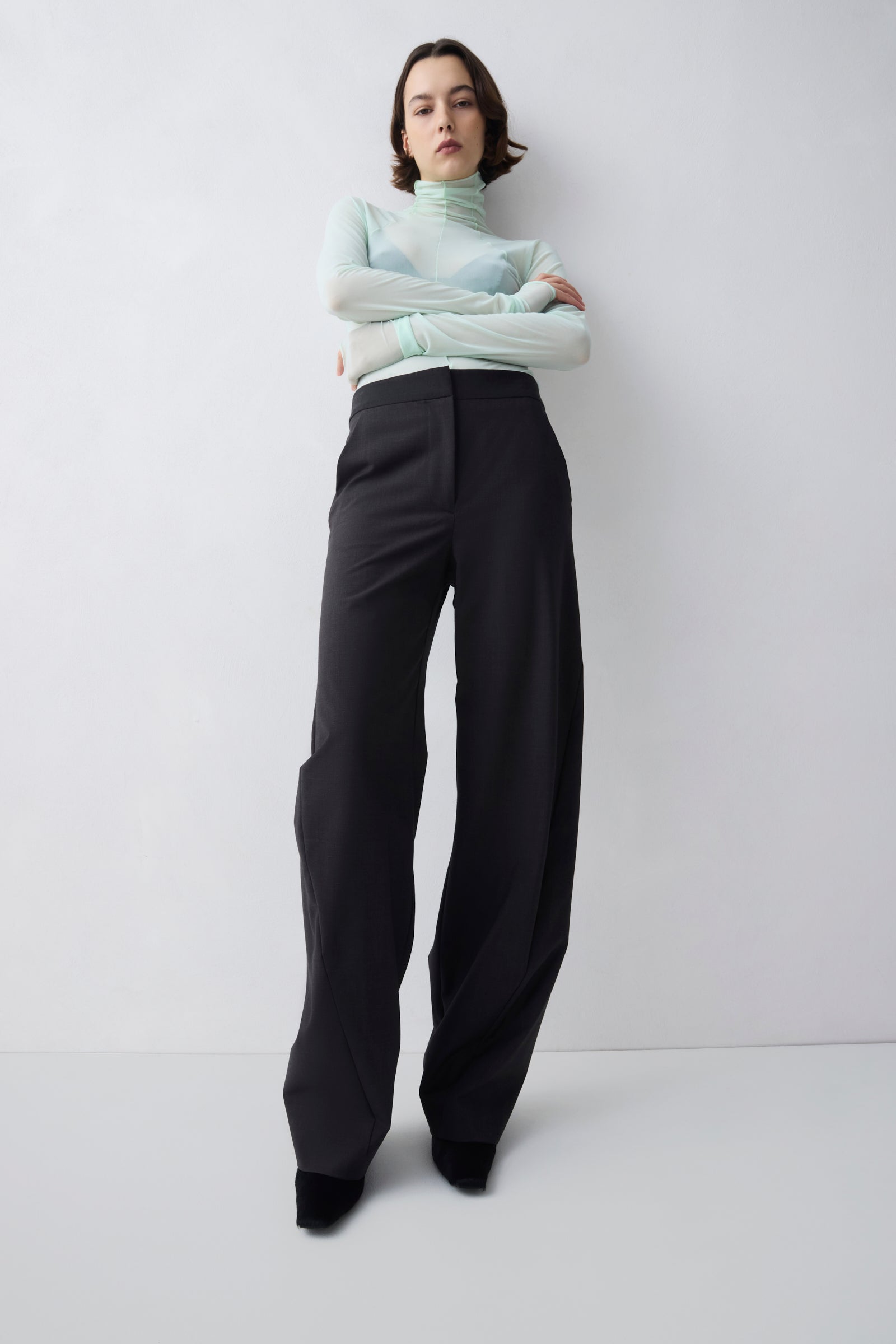 Person wearing a light green turtleneck and black pants against a white background