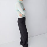 Person wearing a light green sweater and black pants against a white background