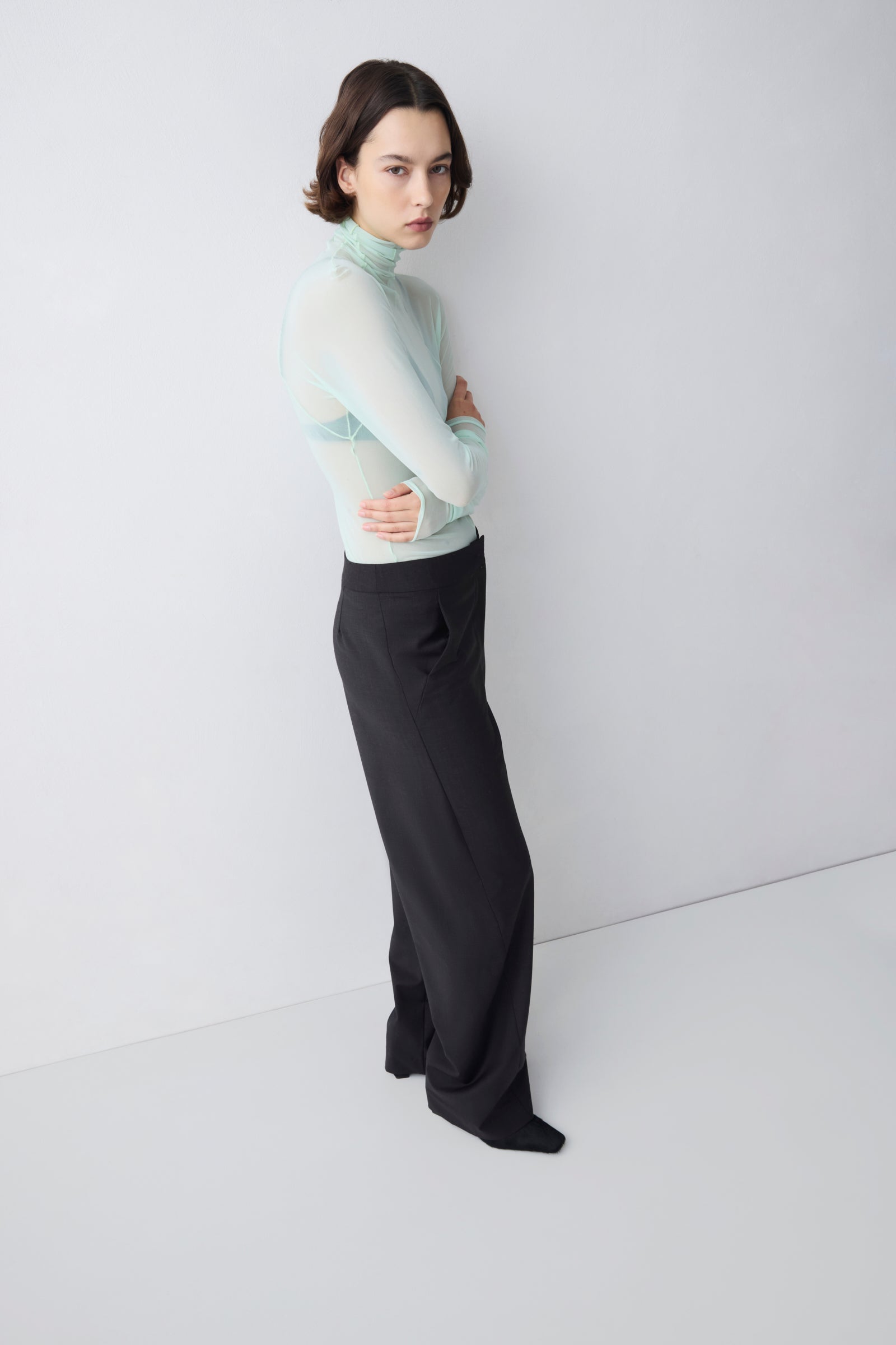 Person wearing a light green sweater and black pants against a white background