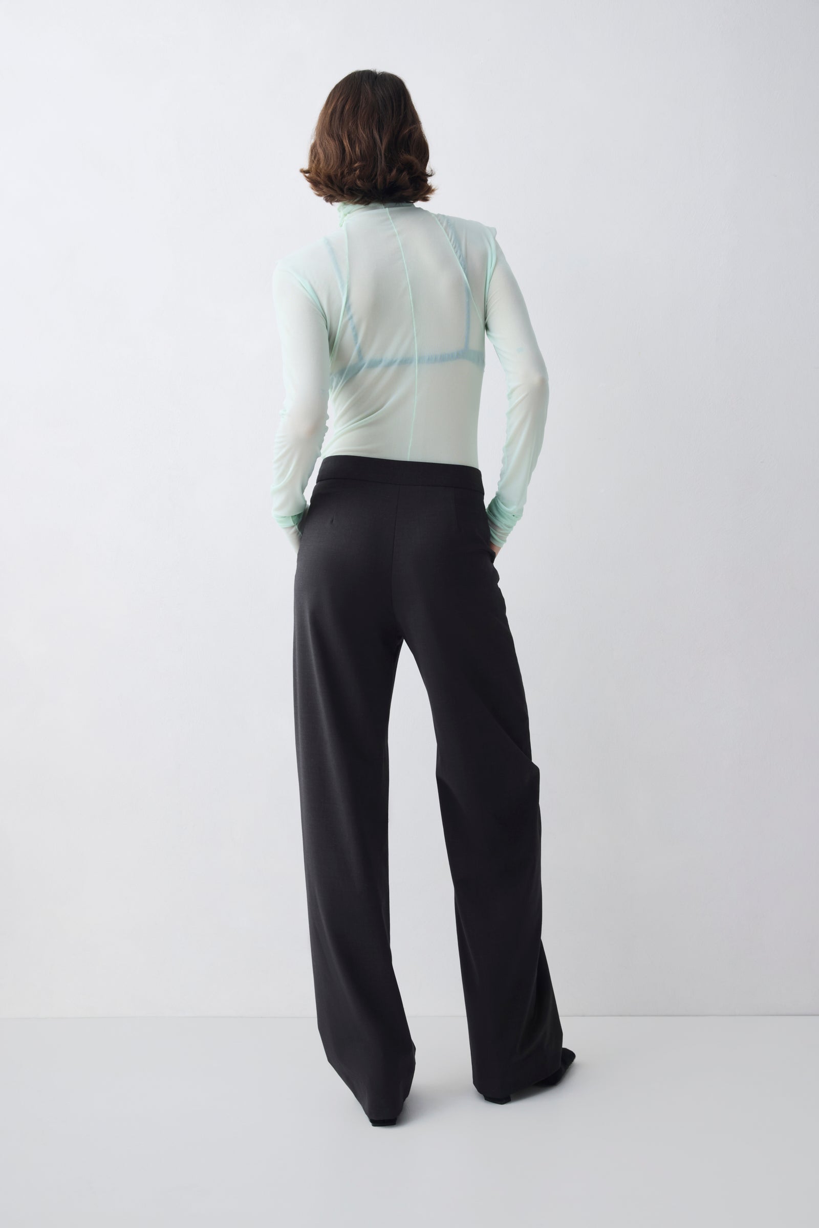 Person wearing a light gray long-sleeve top and black pants on a white background
