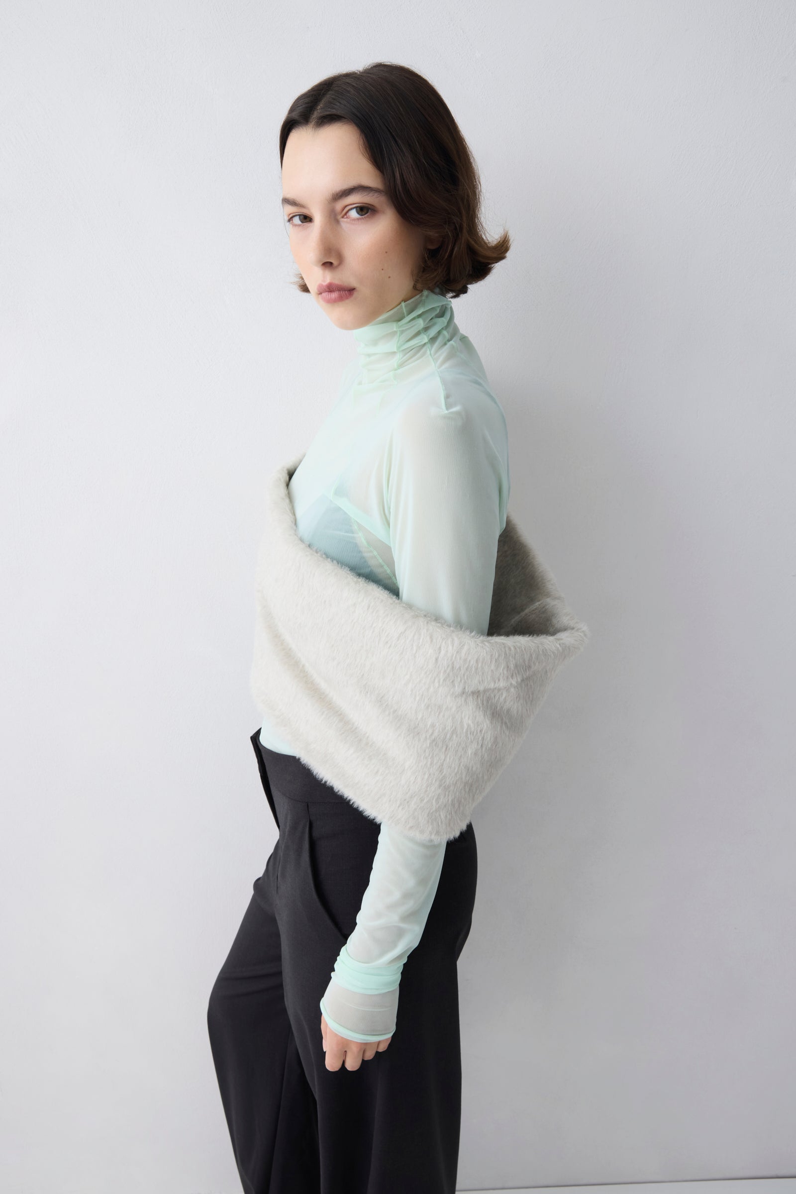 Person wearing a light green turtleneck and black pants with a white background