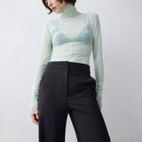 Person wearing a light green turtleneck and black pants on a white background
