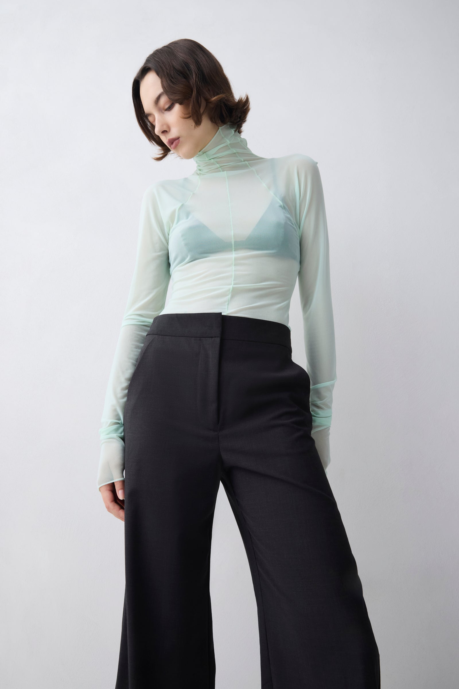 Person wearing a light green turtleneck and black pants on a white background