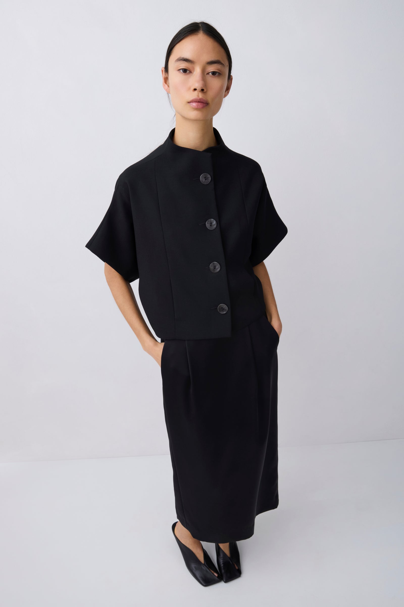 Woman wearing a black outfit with a cape-like top on a white background