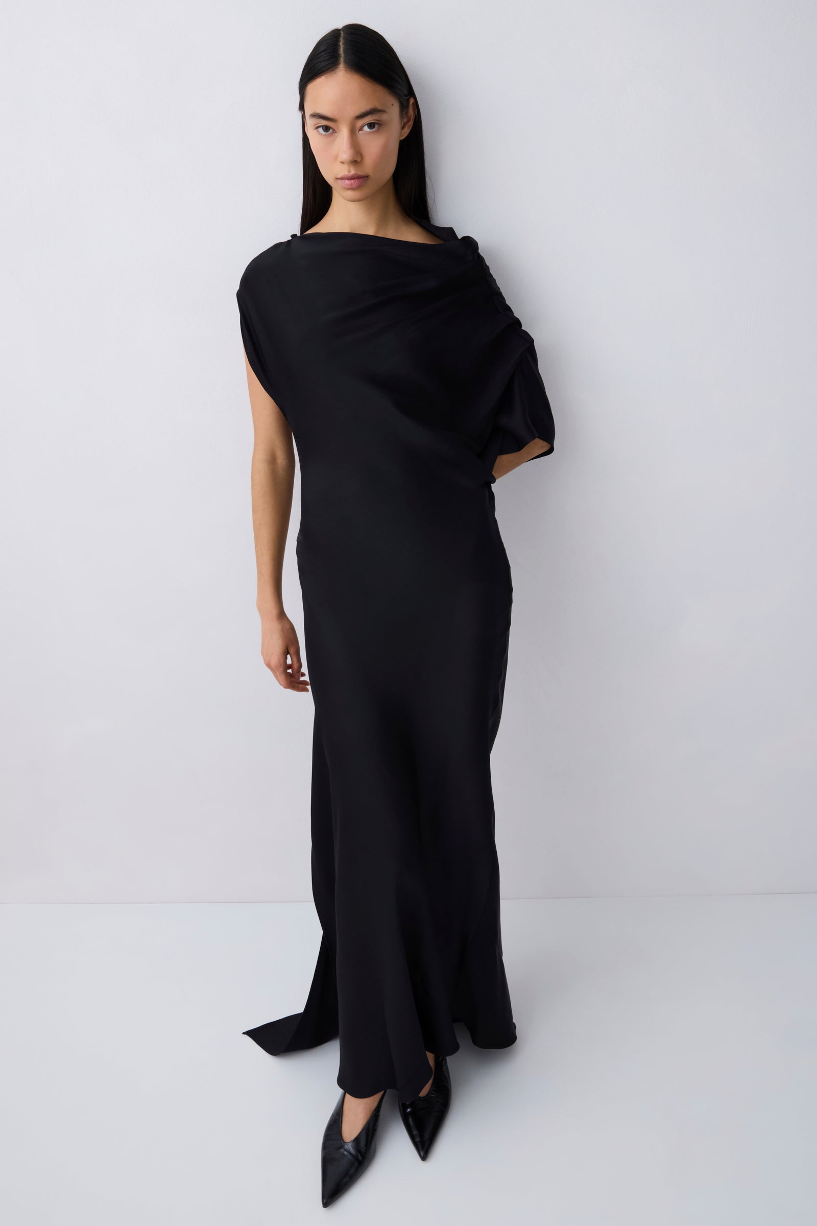 Woman wearing a black one-shoulder dress against a white background