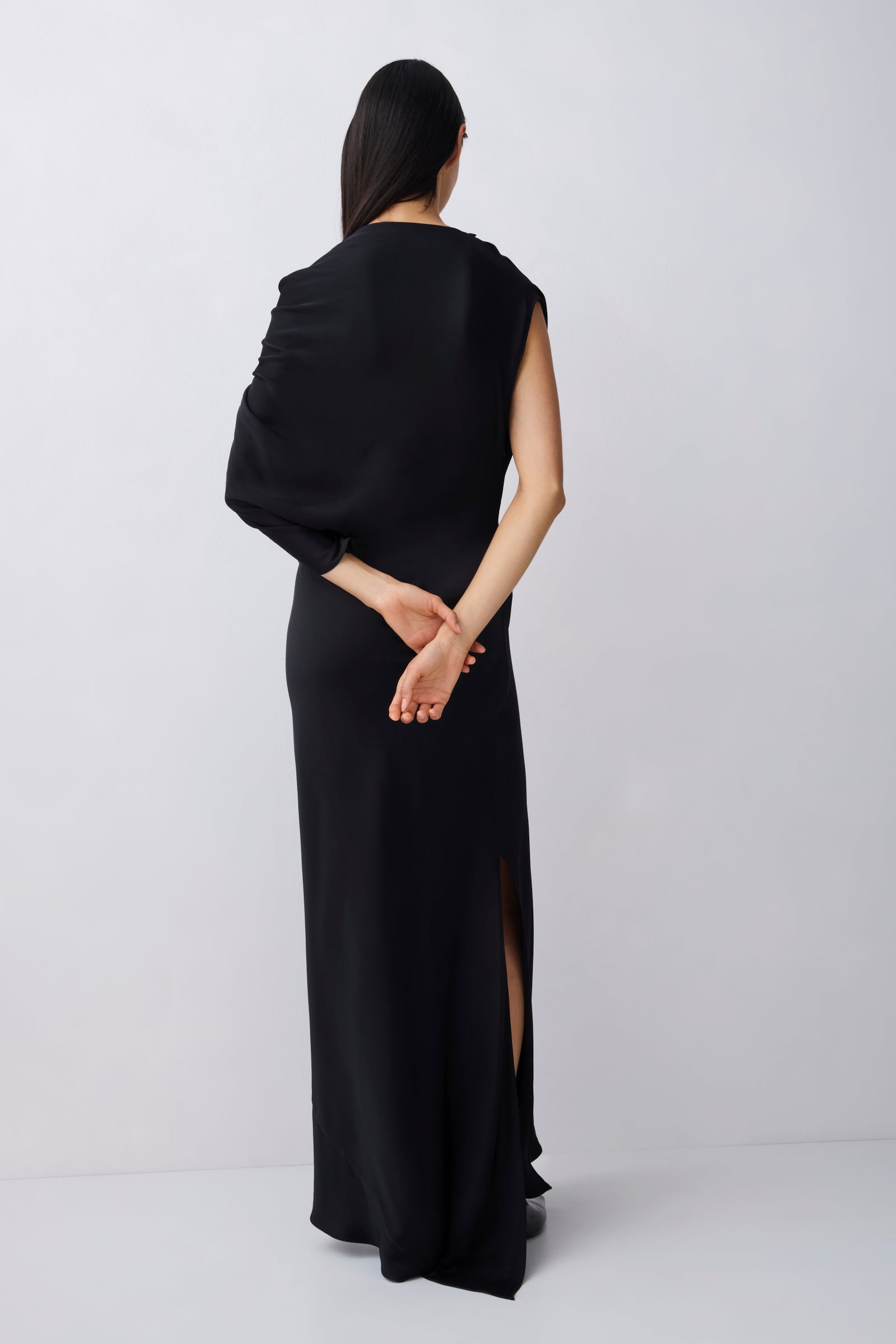 Woman wearing a black sleeveless dress with a draped effect on a white background