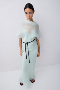 Woman wearing a light green dress with a white top and black belt on a white background