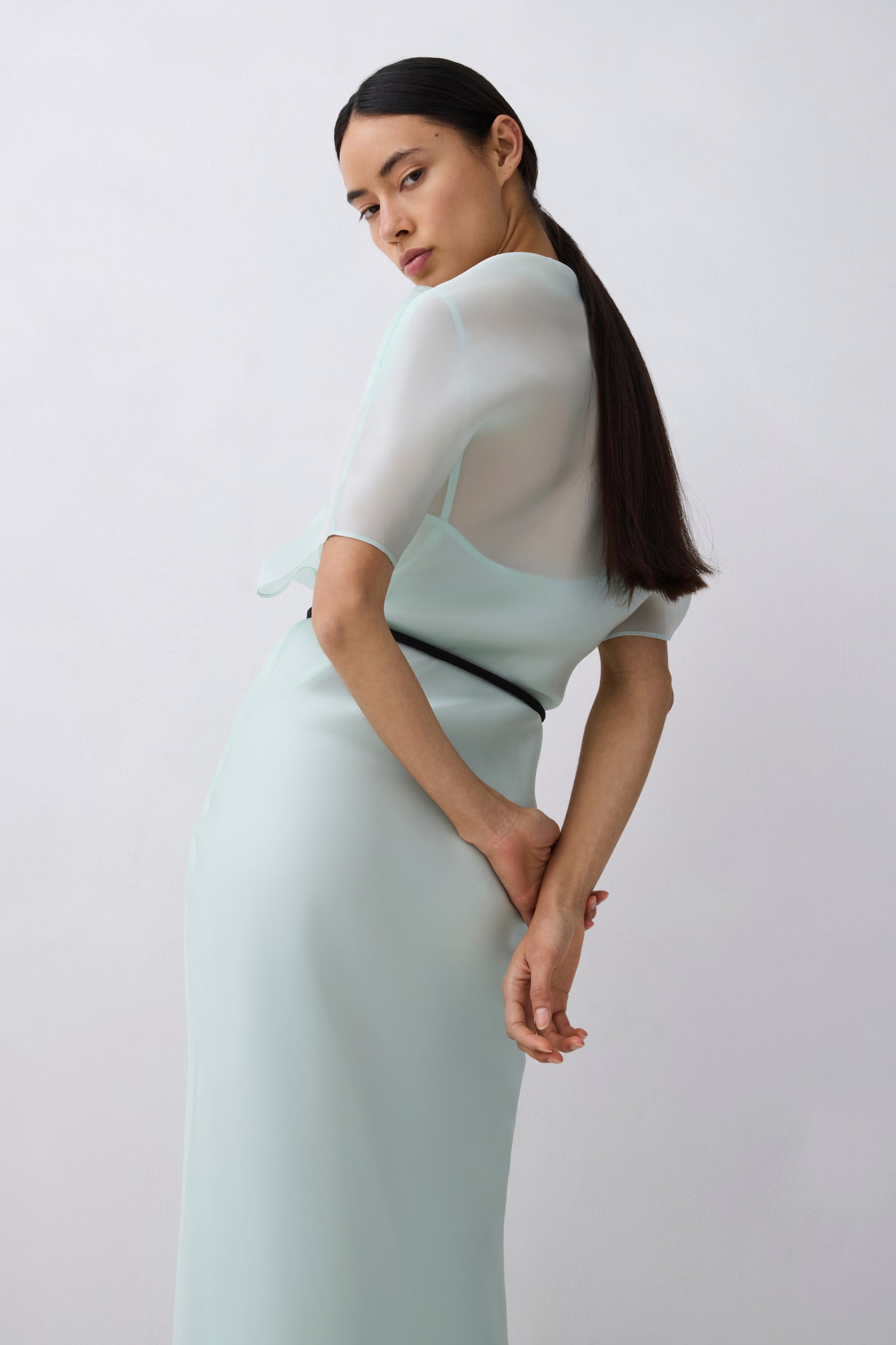 Woman wearing a light green dress with a white top against a plain background
