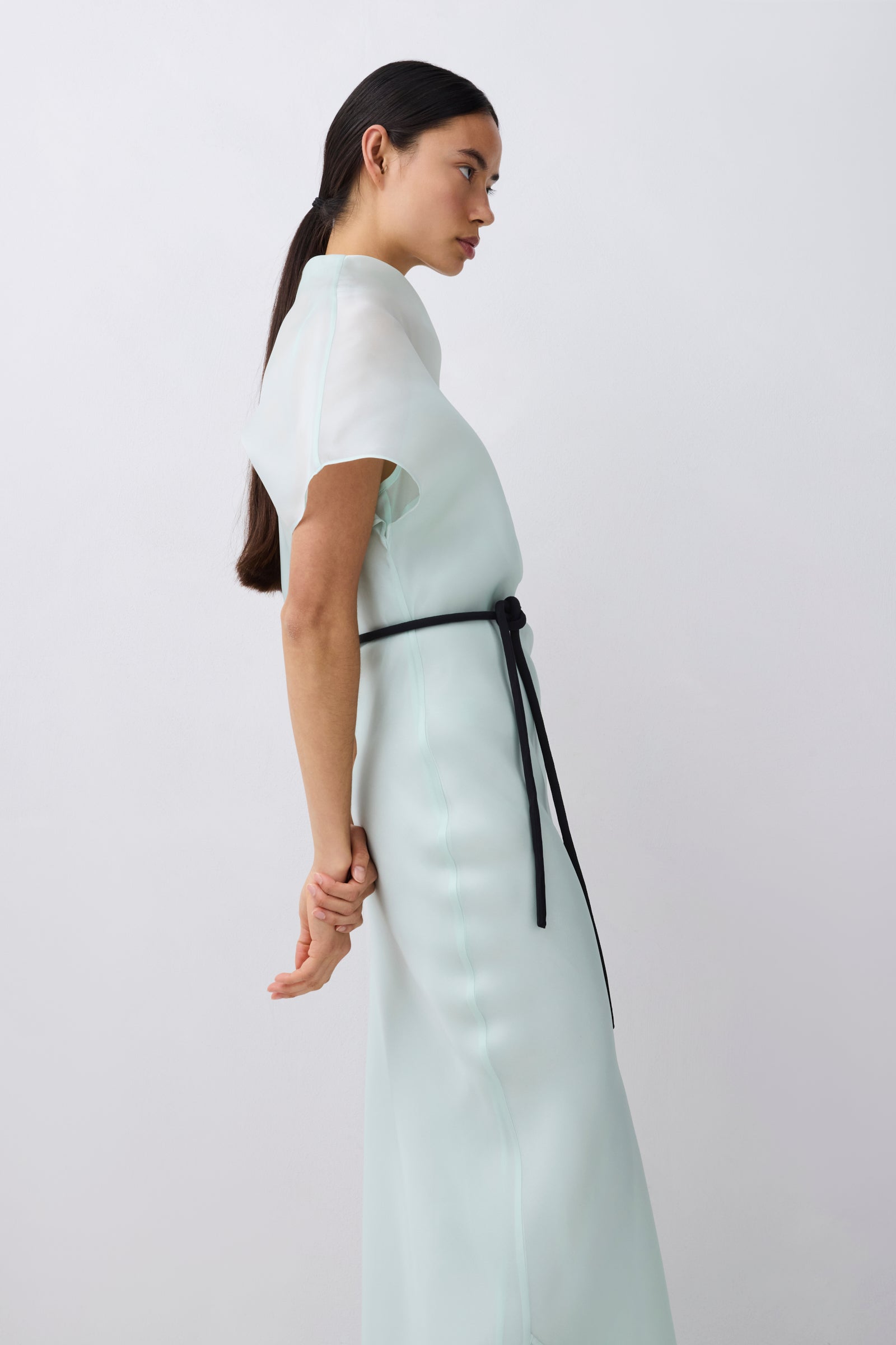 Woman wearing a light-colored dress with a black belt on a white background
