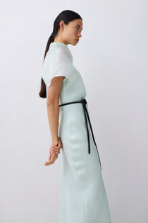 Woman wearing a light-colored dress with a black belt on a white background