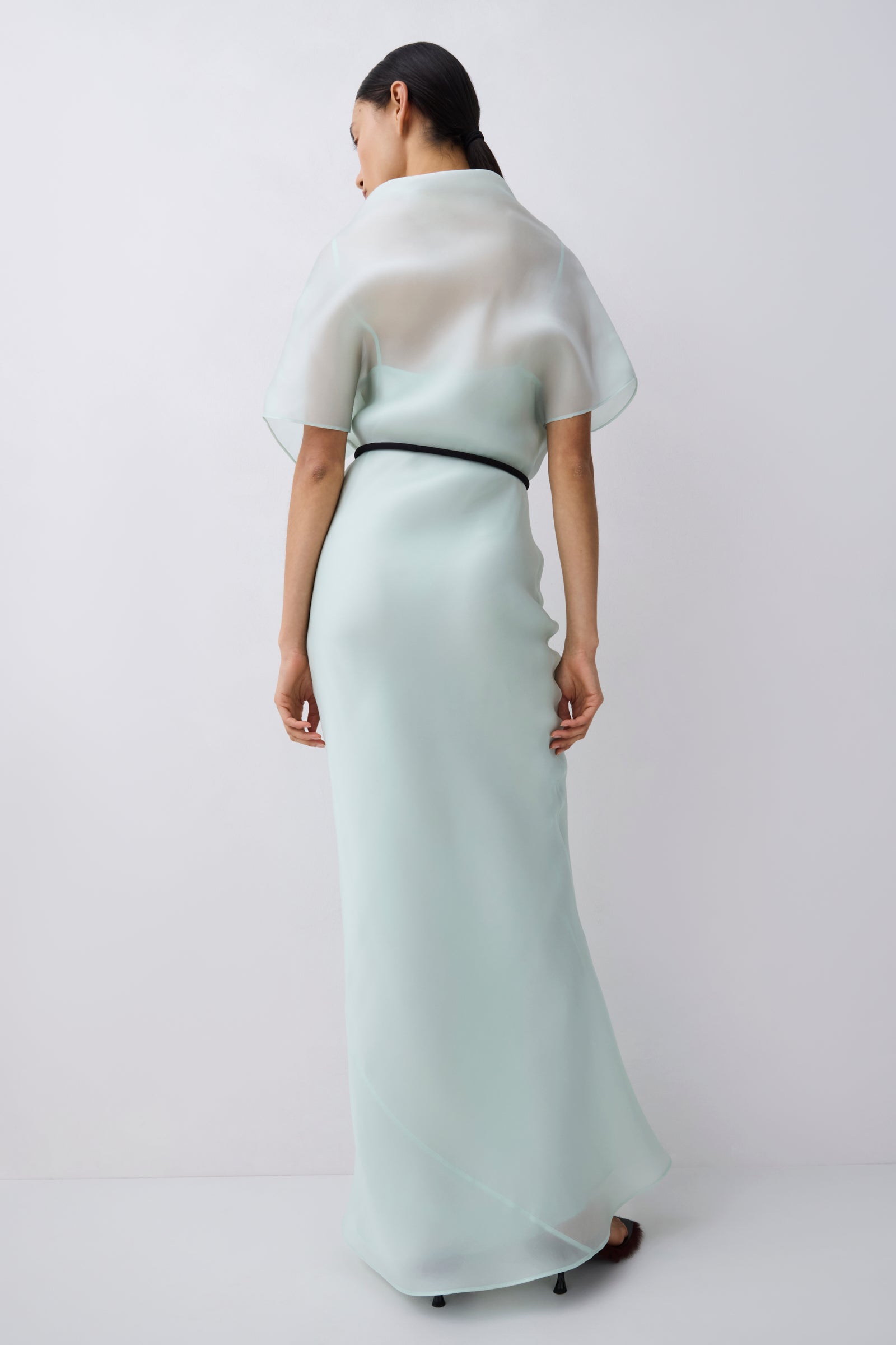Woman wearing a light green dress with a white shawl on a plain background