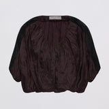 A dark plum purple crinkled blouse with black sheer sleeves, shown from the back against a light gray background.