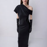 A model wearing a black one-shoulder satin dress with long black gloves, standing against a light gray studio background.