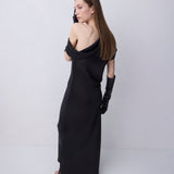 A woman modeling a black off-the-shoulder maxi dress with long black gloves, photographed from the back against a plain light gray studio background.
