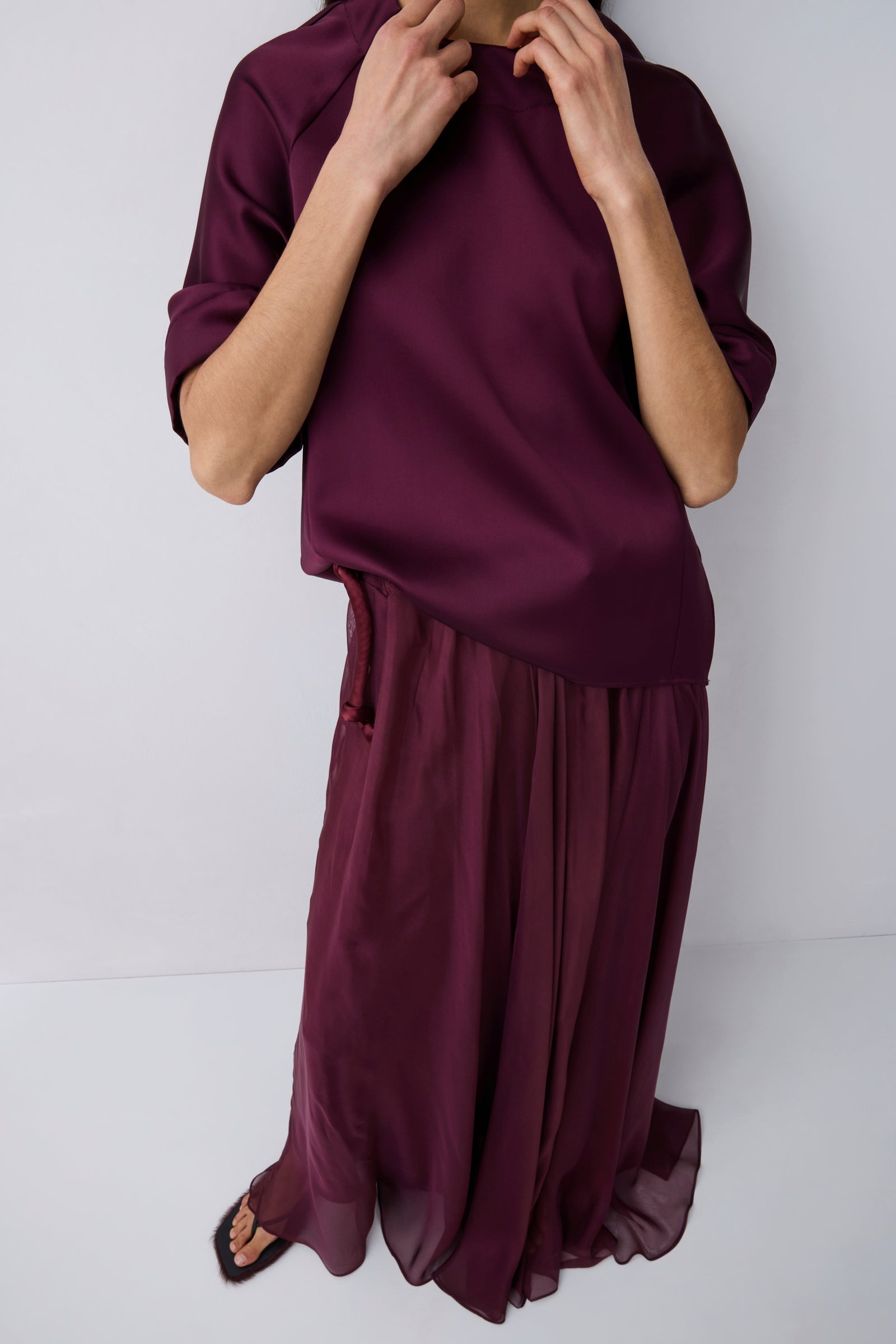 Person wearing a burgundy outfit with a top and flowing pants on a white background