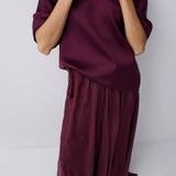 Person wearing a burgundy outfit with a top and flowing pants on a white background