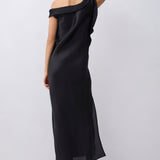 A woman wearing a black off-the-shoulder maxi dress with a side slit, shown from the back against a light gray studio background.