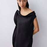 A woman modeling a black off-the-shoulder cowl-neck dress against a light gray studio background.