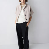Woman wearing a light beige jacket over a white sweater and black pants on a white background