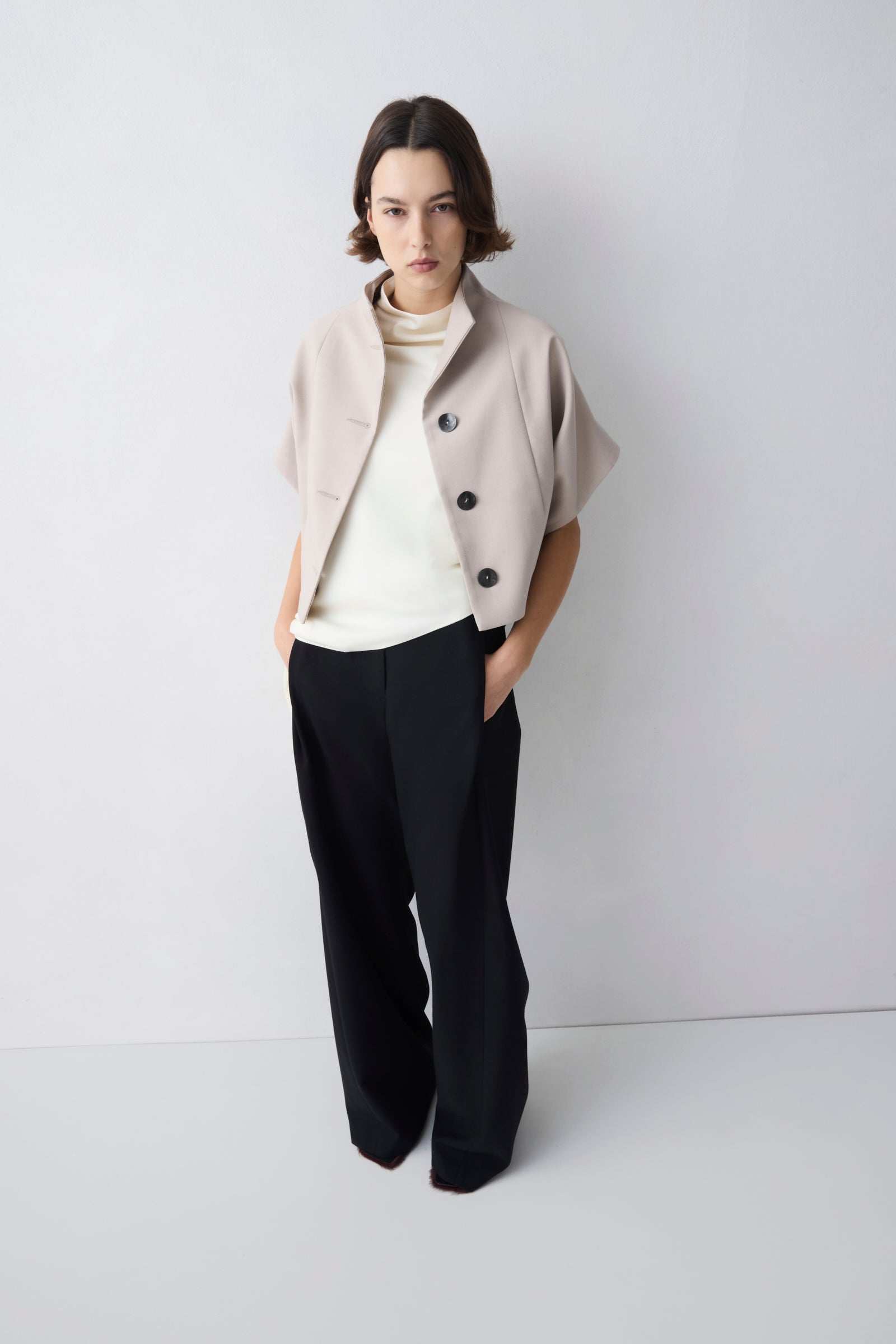 Woman wearing a light beige jacket over a white sweater and black pants on a white background