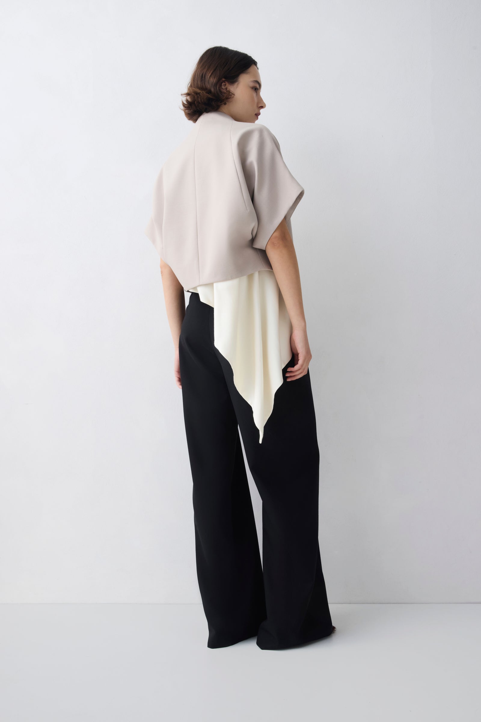 Person wearing a beige top and black pants against a white background