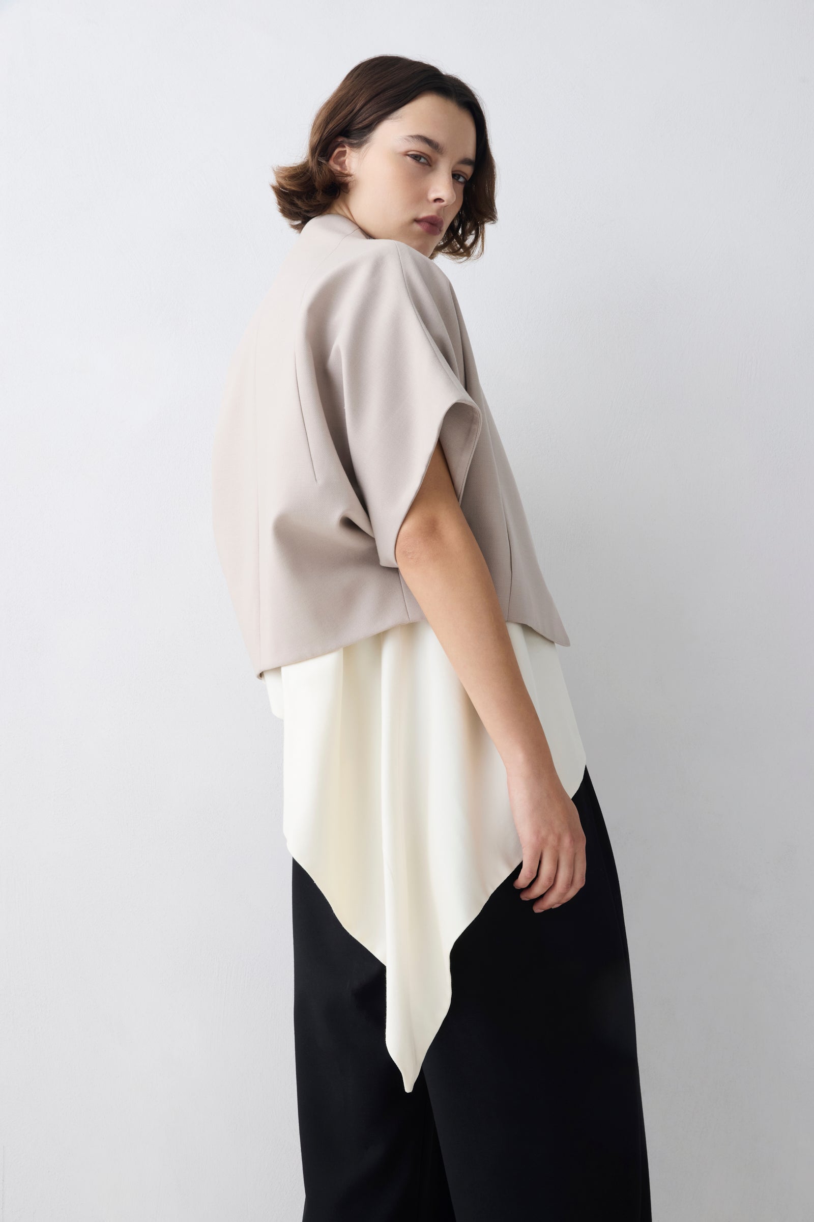 Woman wearing a beige and white layered top against a plain background
