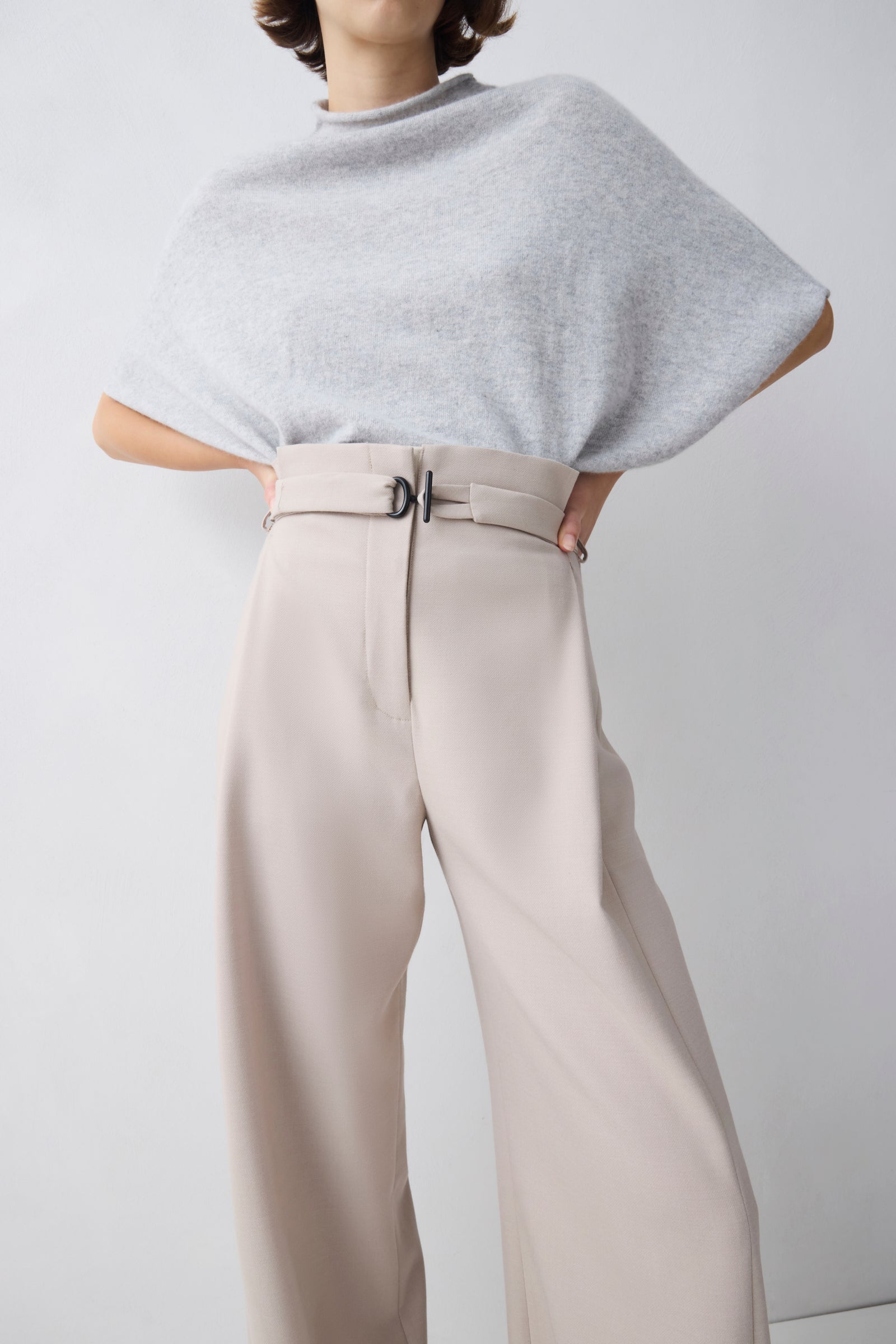 Person wearing a light gray poncho and beige pants on a white background