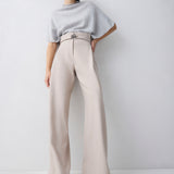 Woman wearing a light gray sweater and beige wide-leg pants on a white background
