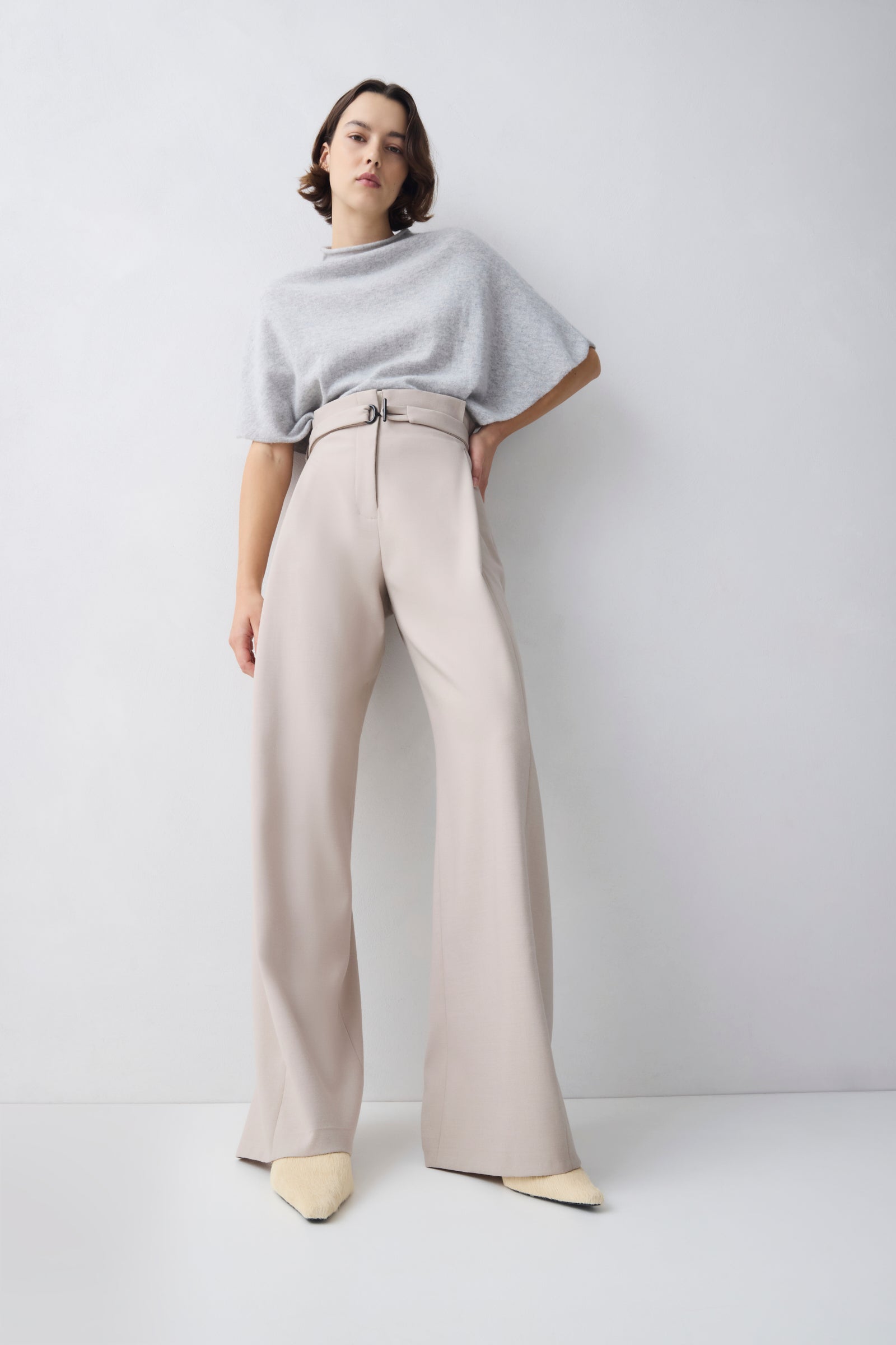 Woman wearing a light gray sweater and beige wide-leg pants on a white background
