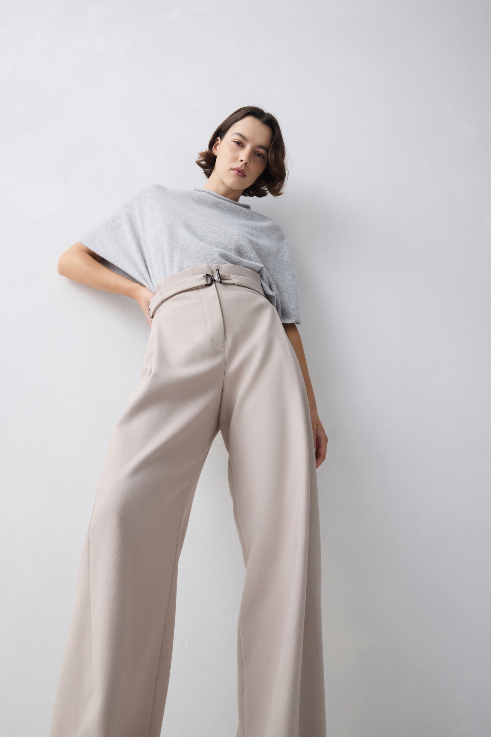 Person wearing a light gray top and beige pants against a white background