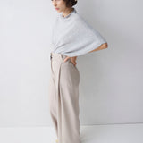 Woman wearing a light gray poncho and beige pants against a white background