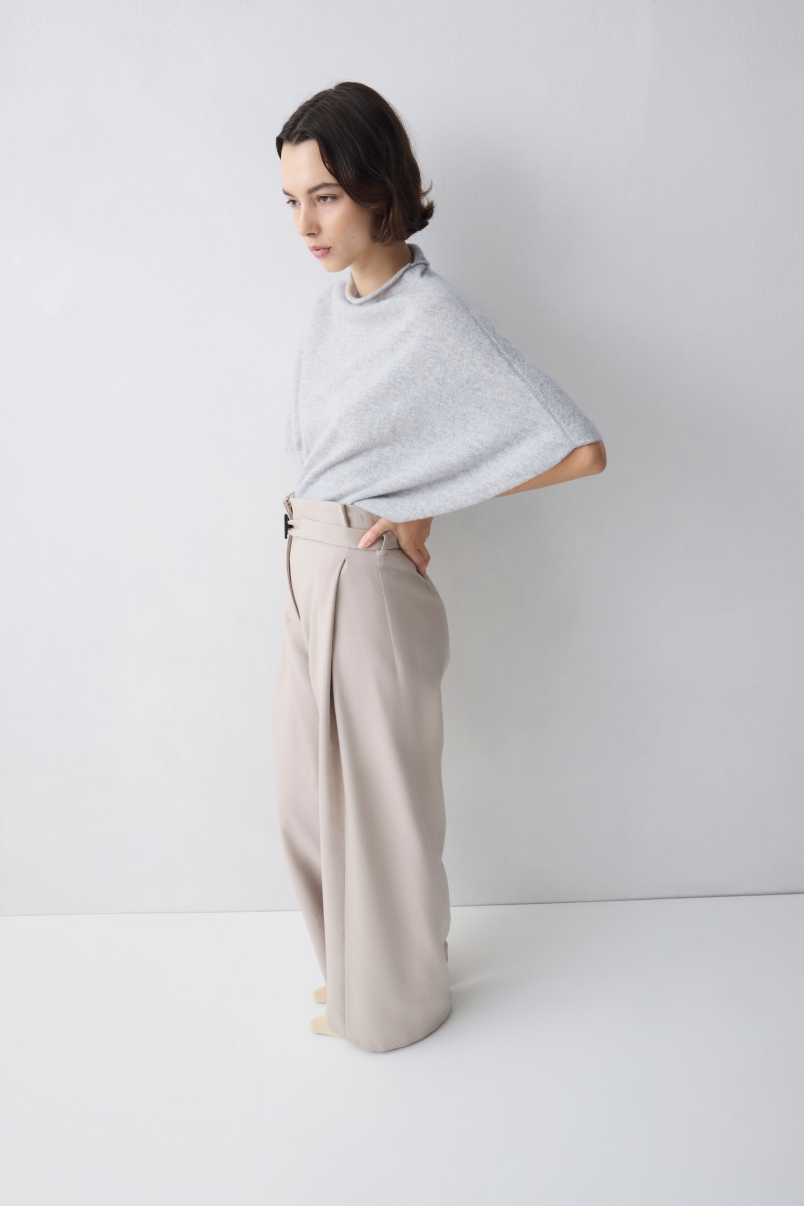 Woman wearing a light gray poncho and beige pants against a white background