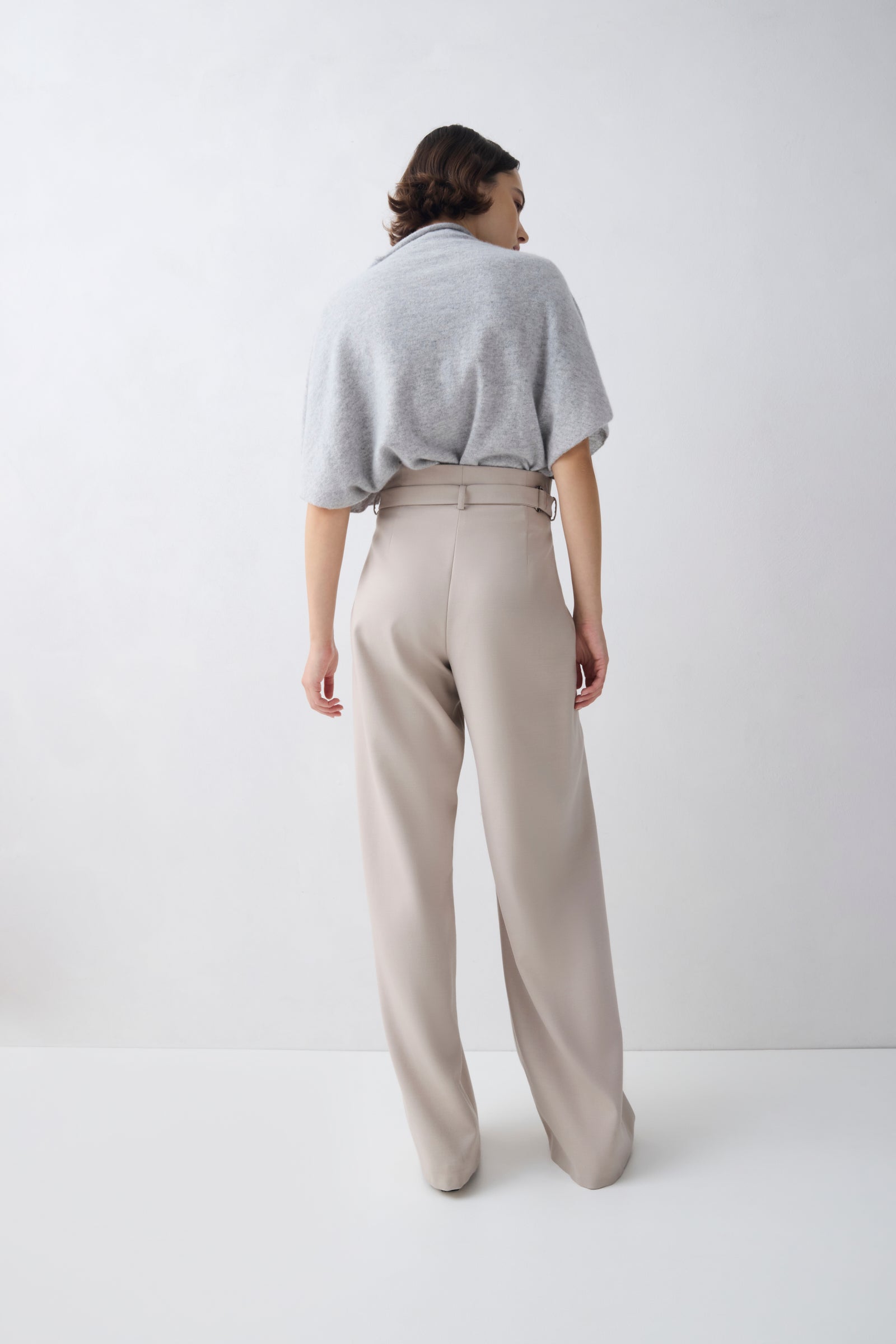 Person wearing a light gray sweater and beige pants on a white background
