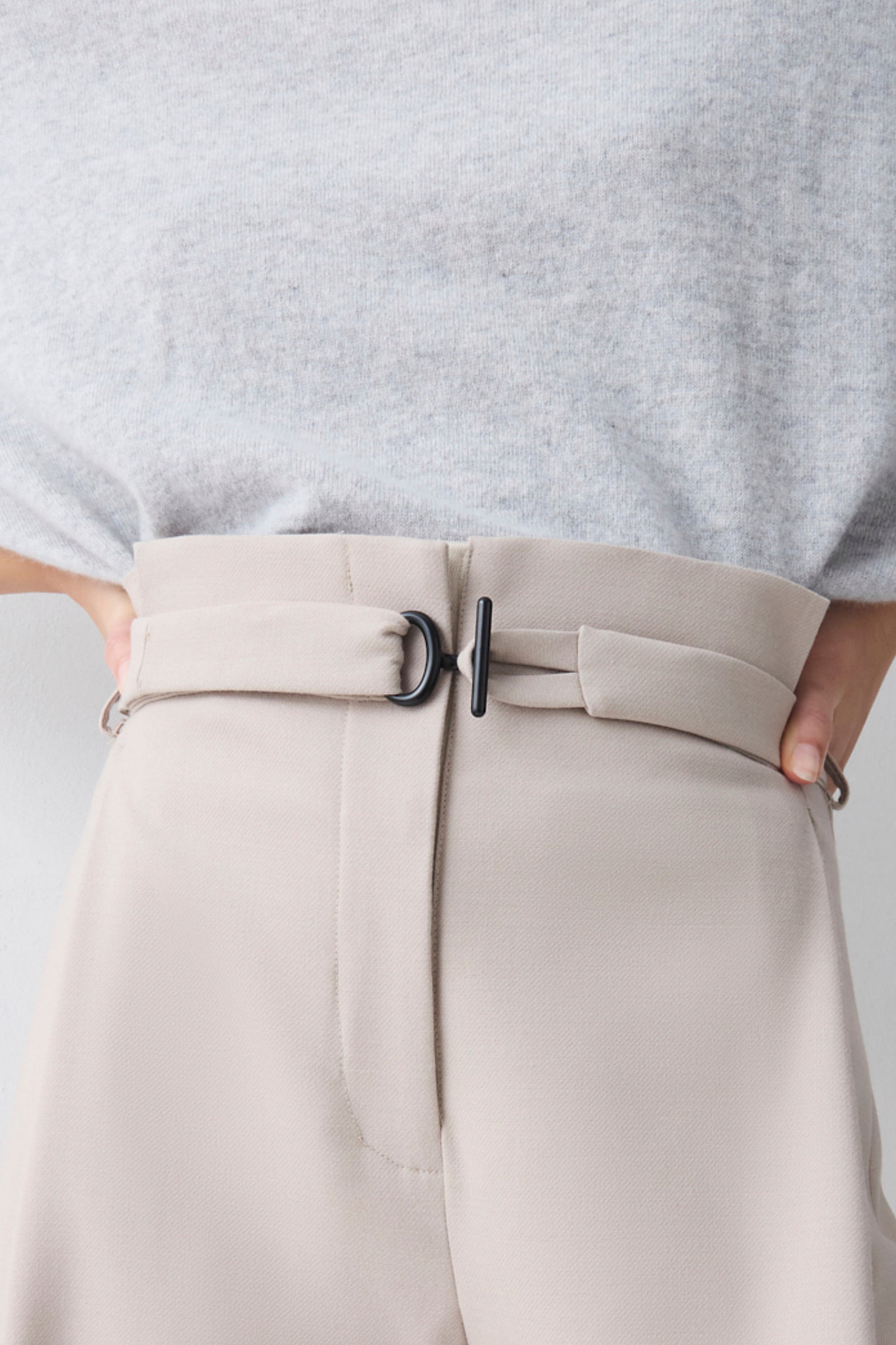 Beige pants with a belt and gray top on a light gray background