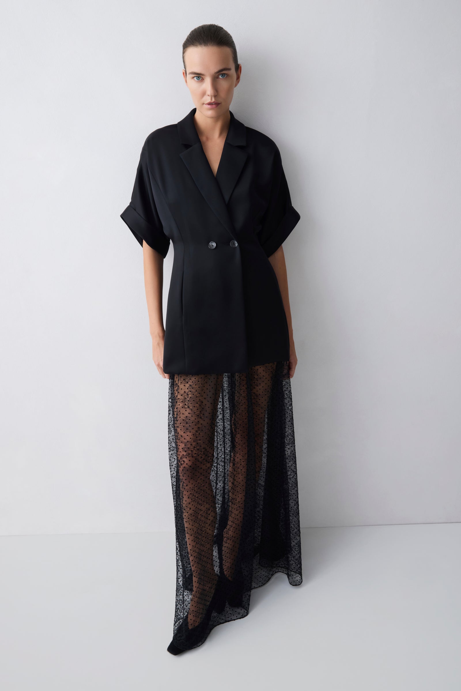 Model wearing a black outfit with a jacket and sheer skirt on a white background