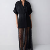 Model wearing a black outfit with a jacket and sheer skirt on a white background