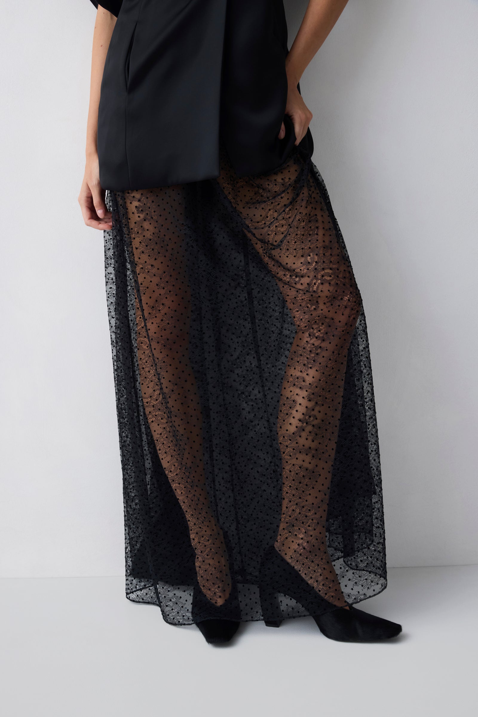 Person wearing a black outfit with sheer black lace overlay on a white background