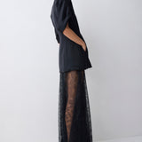 Woman wearing a black outfit with sheer overlay on a white background
