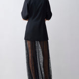 Person wearing a black coat over a sheer black skirt on a white background