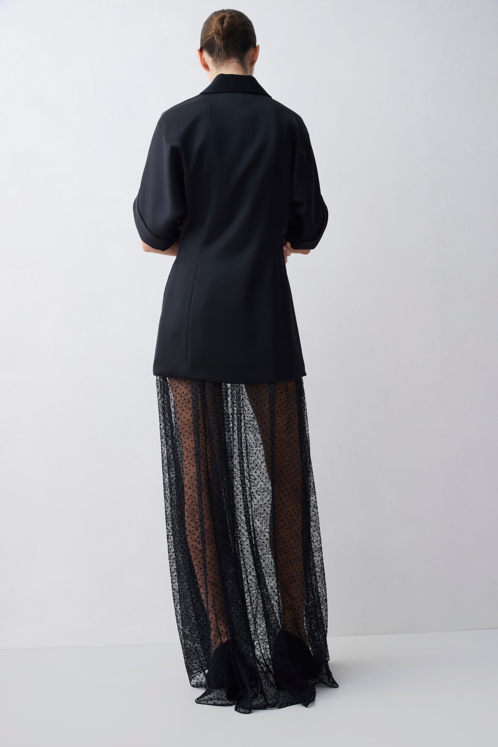 Person wearing a black coat over a sheer black skirt on a white background