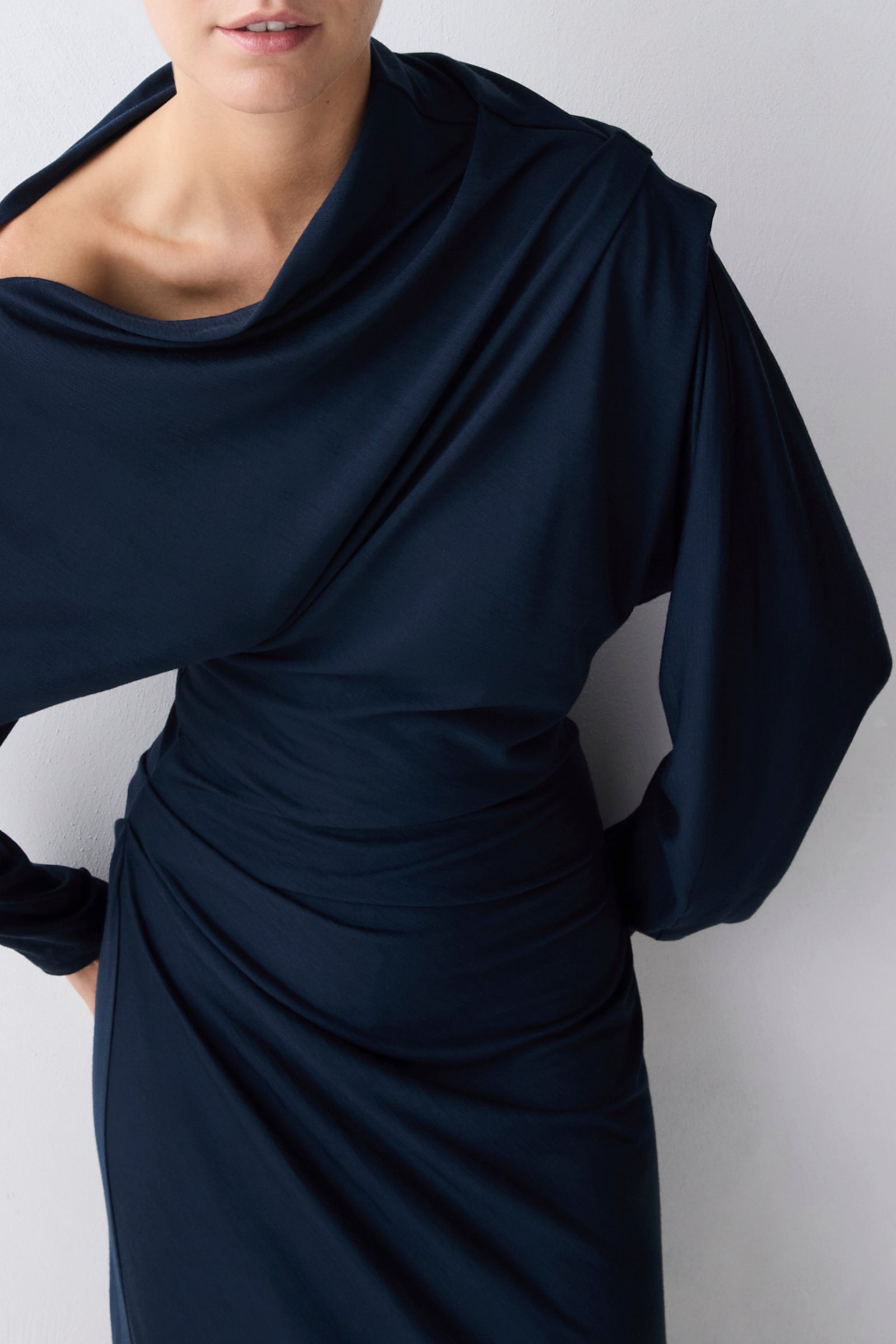 Navy blue draped dress worn by a person on a white background