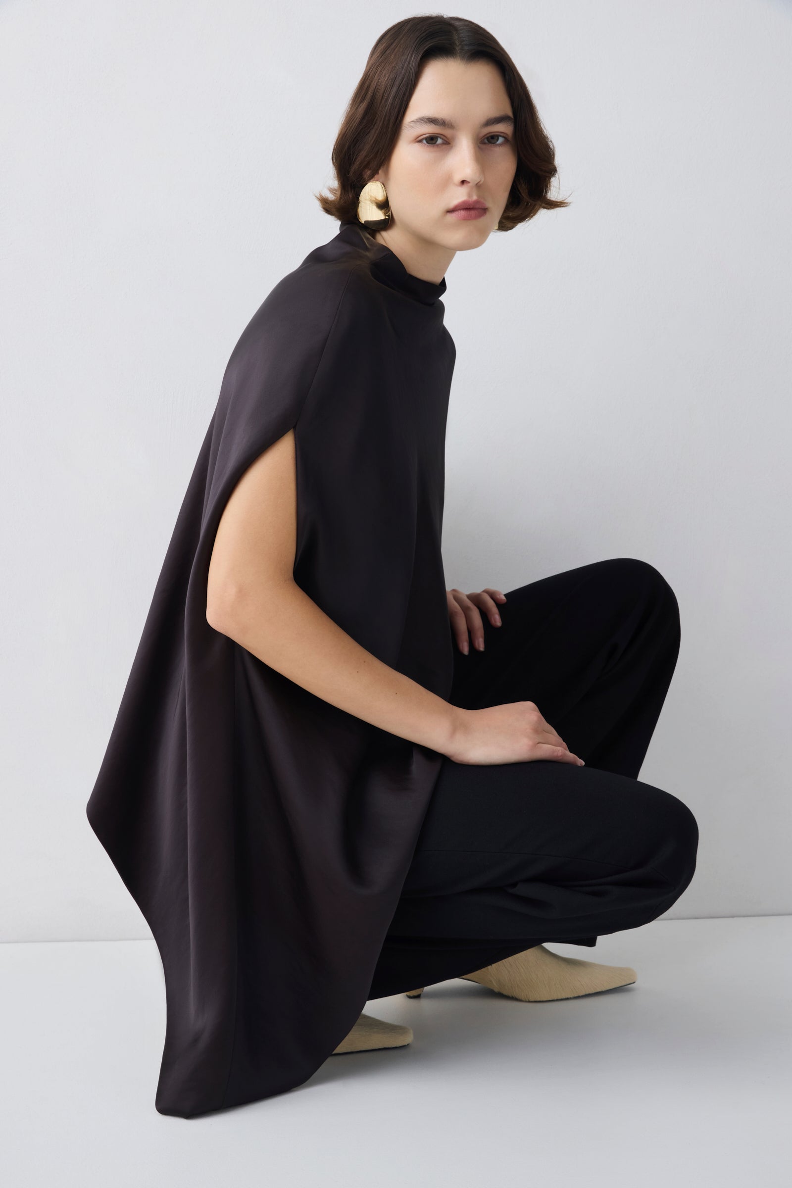 Person wearing a black outfit with a cape on a white background