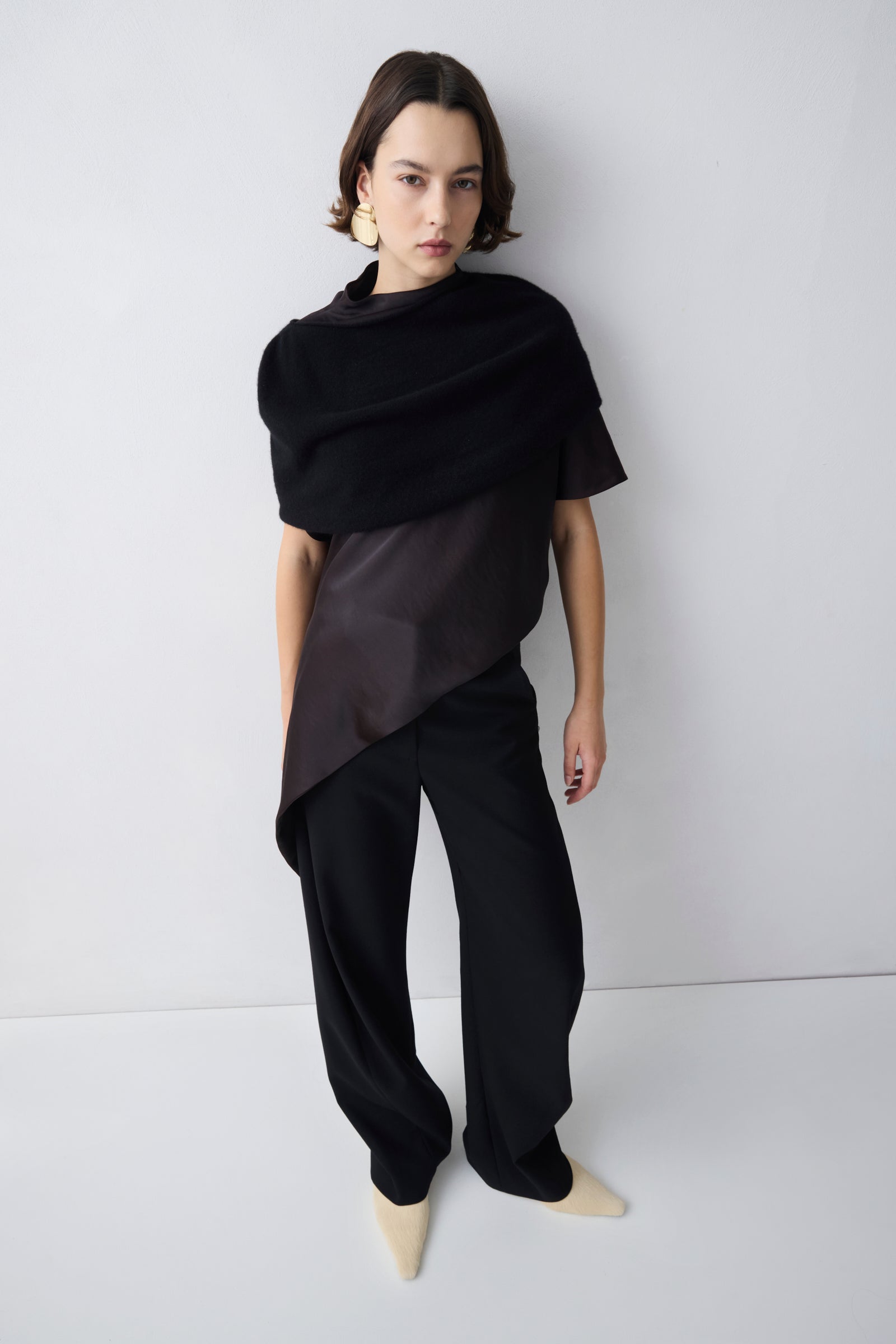 Person wearing a black outfit with a draped top against a white background
