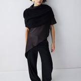 Person wearing a black outfit with a draped top against a white background