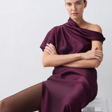 Woman wearing a burgundy off-shoulder dress sitting on a white stool against a light gray background