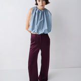 Woman wearing a light blue sleeveless top and dark purple pants on a white background
