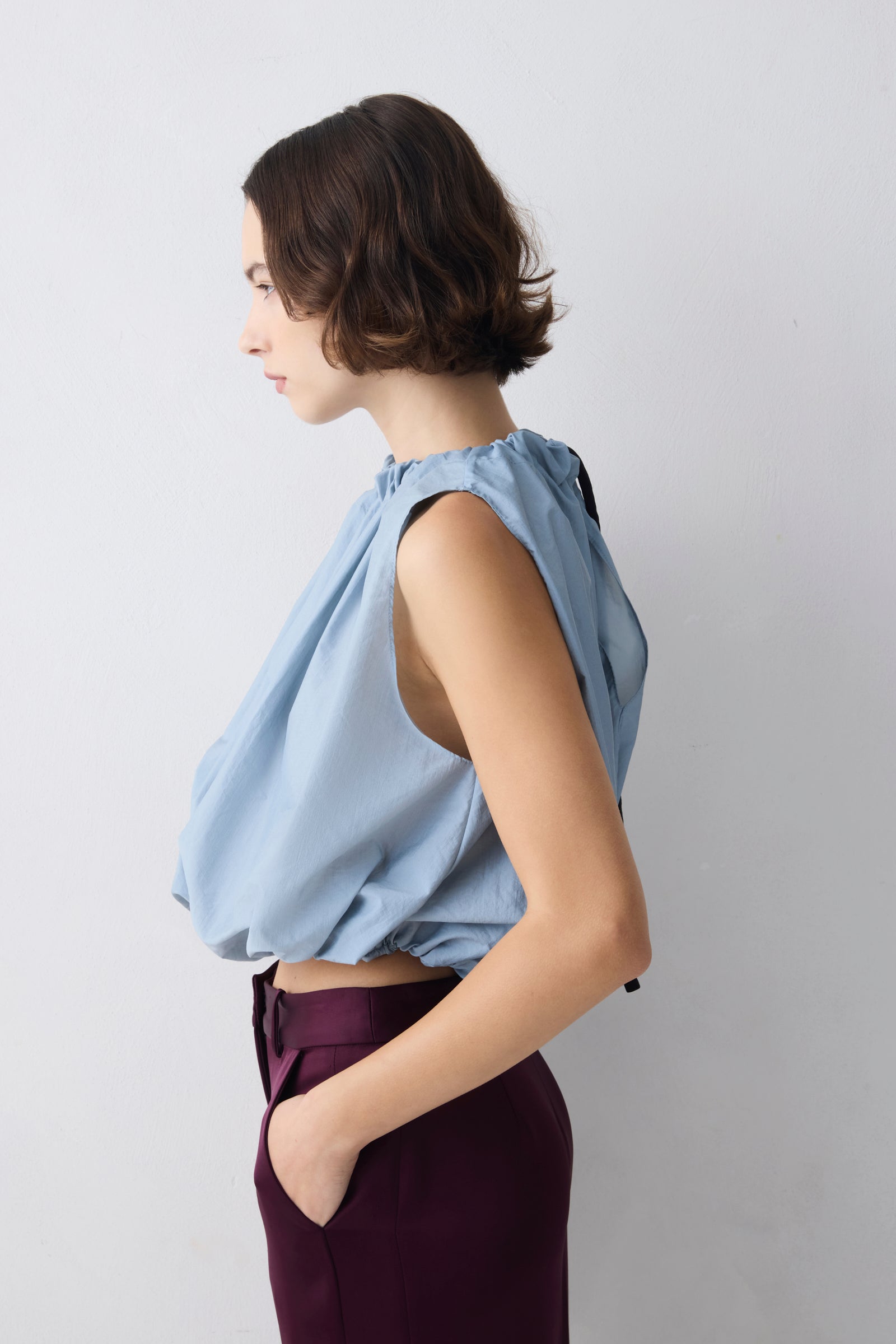Woman wearing a light blue sleeveless top and dark purple pants against a plain background