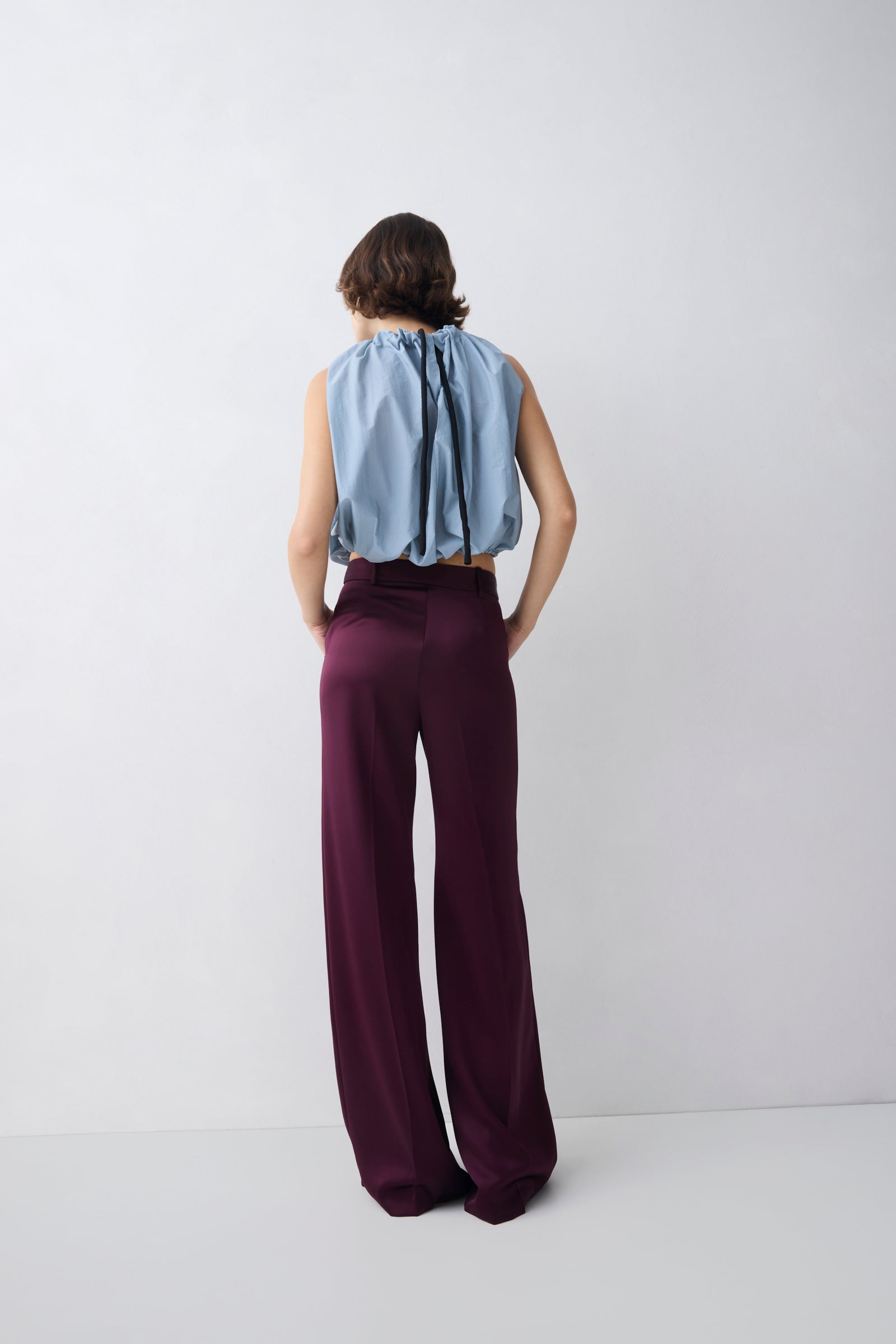 Person wearing a light blue sleeveless top and dark purple wide-leg pants on a white background